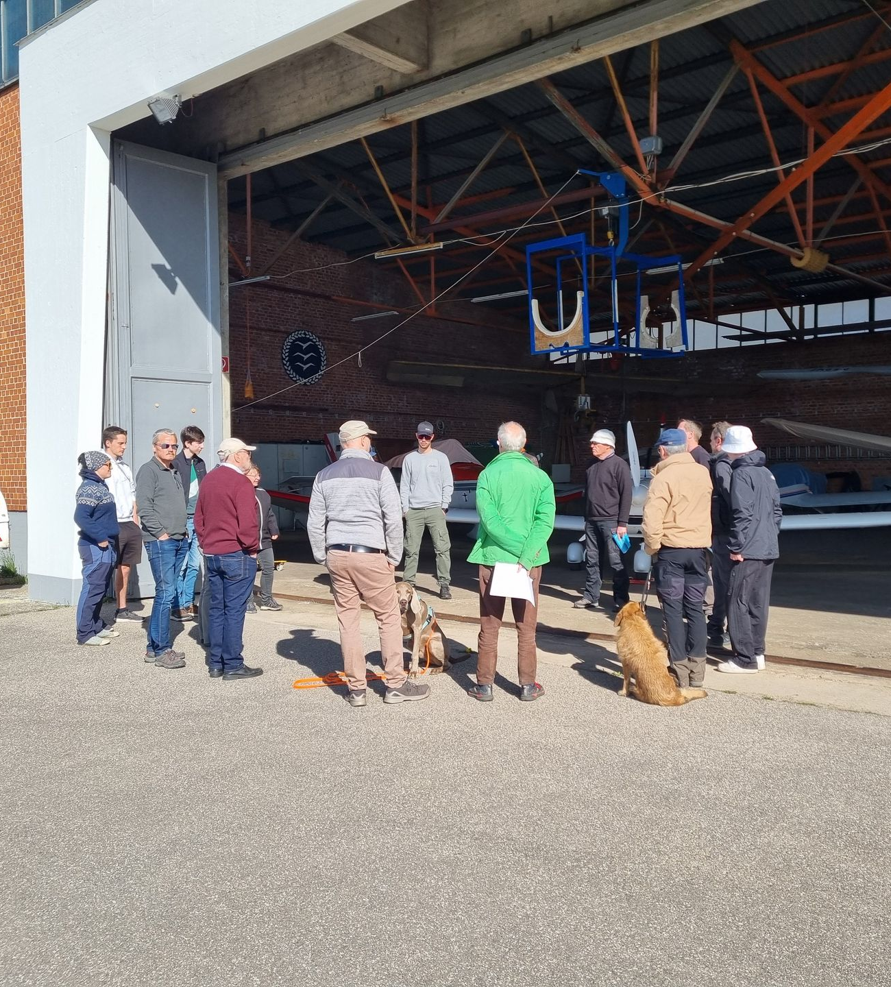Mehrere Personen stehen im Kreis vor einem Flugzeughangar.