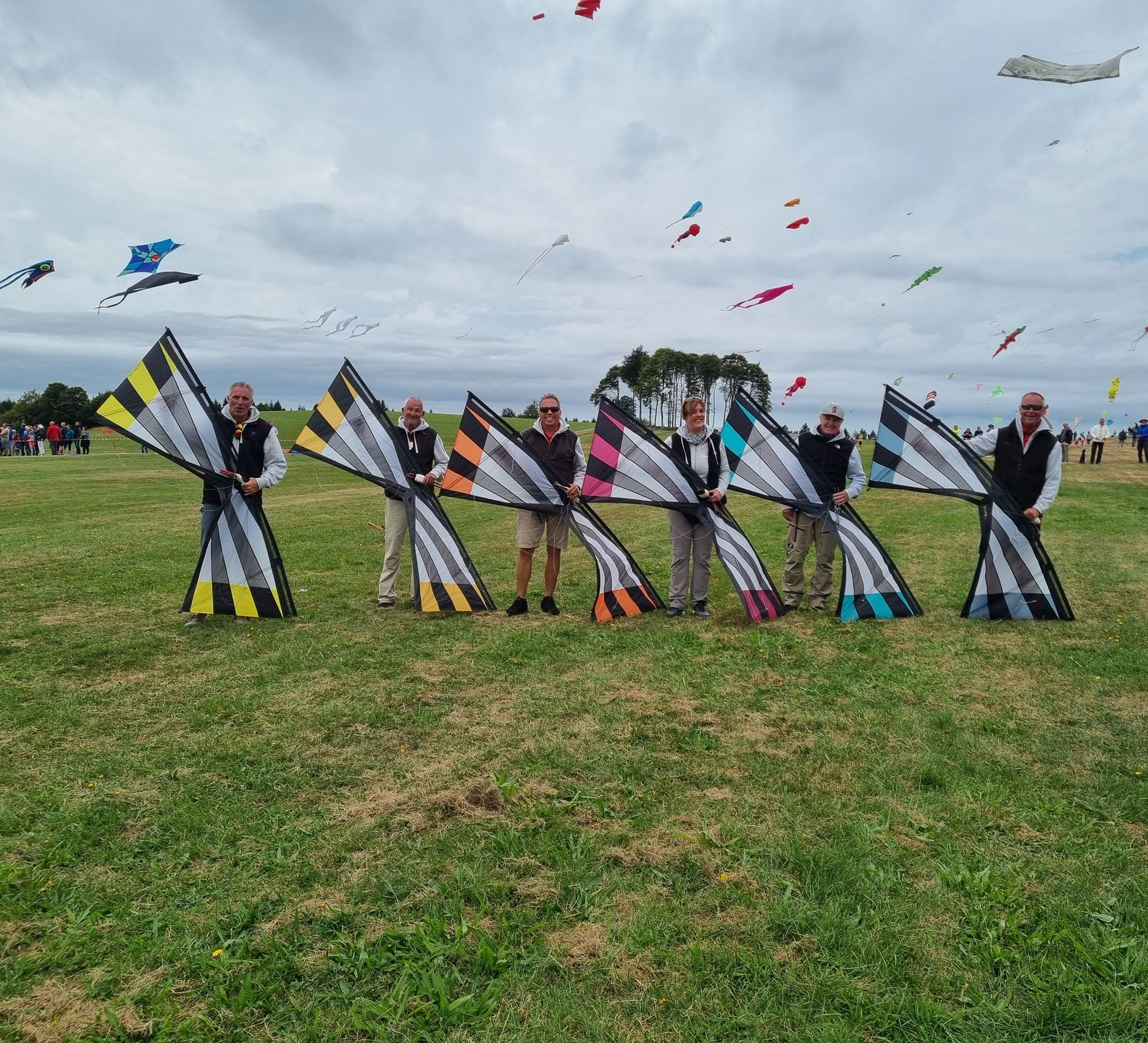 Sechs Personen halten jeweils gleichartig gestaltete, aber unterschiedlich farbige 4-LeinerDrachen .