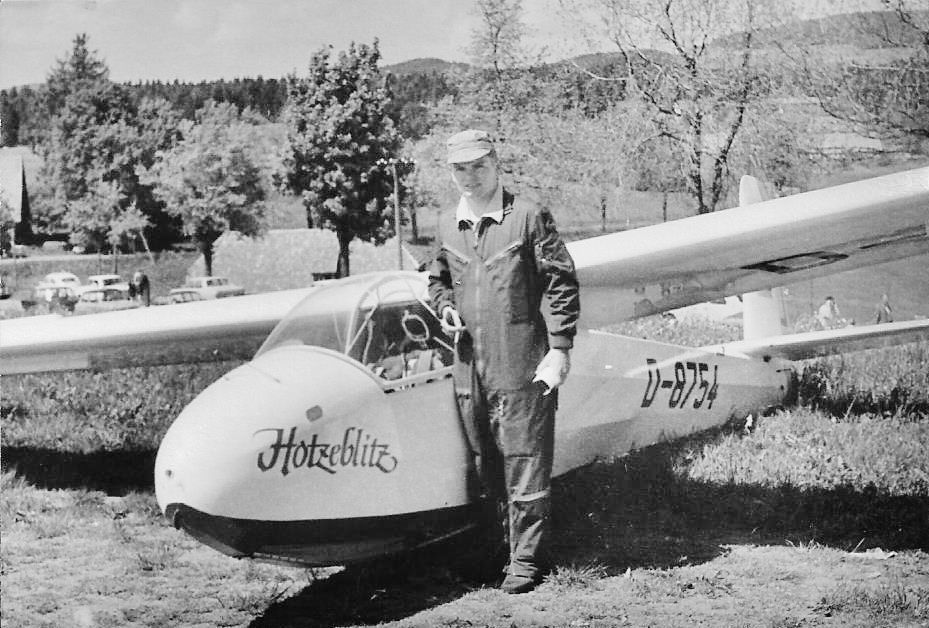 Schwarz-weiß-Aufnahme eines historischen Segelflugzeugs mit der Aufschrift Hotzeblitz, der Pilot steht im Overall daneben.