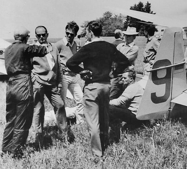 Schwarz-weiß-Aufnahme: Mehrere Männer stehen herum, ein Segelflugzeug-Leitwerk ragt von rechts ins Bild.