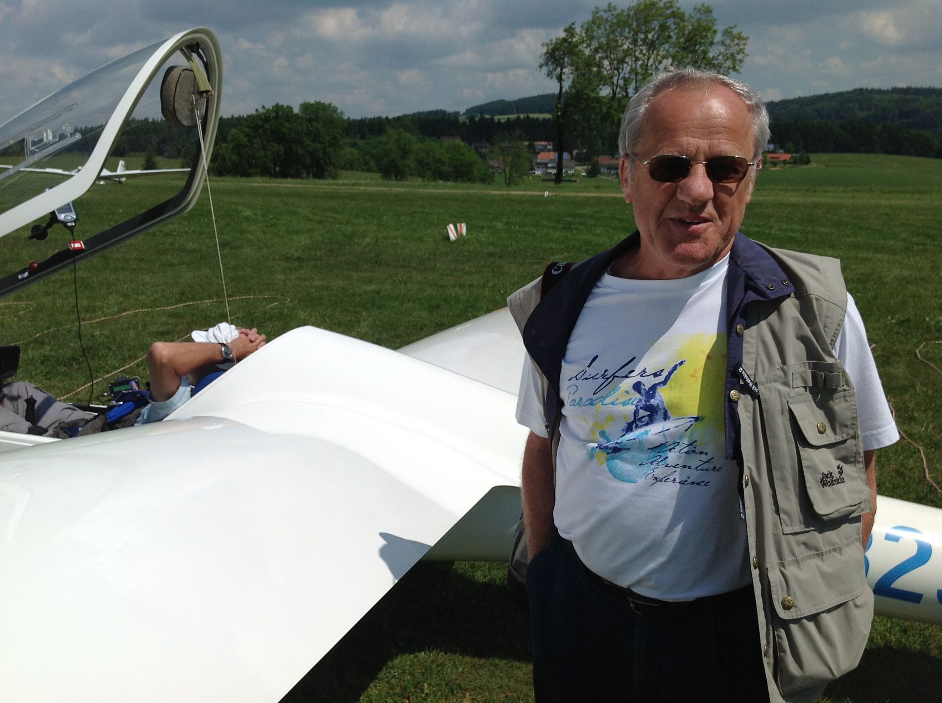 Eine Person steht hinter einem Segelflugzeug, indem jemand sitzt und das die Haube offen hat.