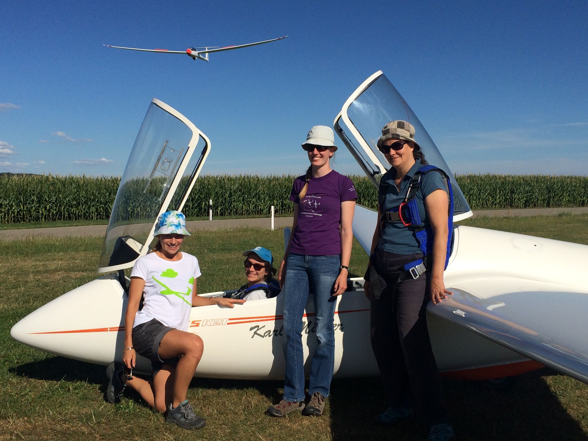 Ein Doppelsitziges Segelflugzeug mit offener Haube. Vier Frauen, eine sitzt auf dem Pilotensitz, drei stehen vor dem Flugzeug.