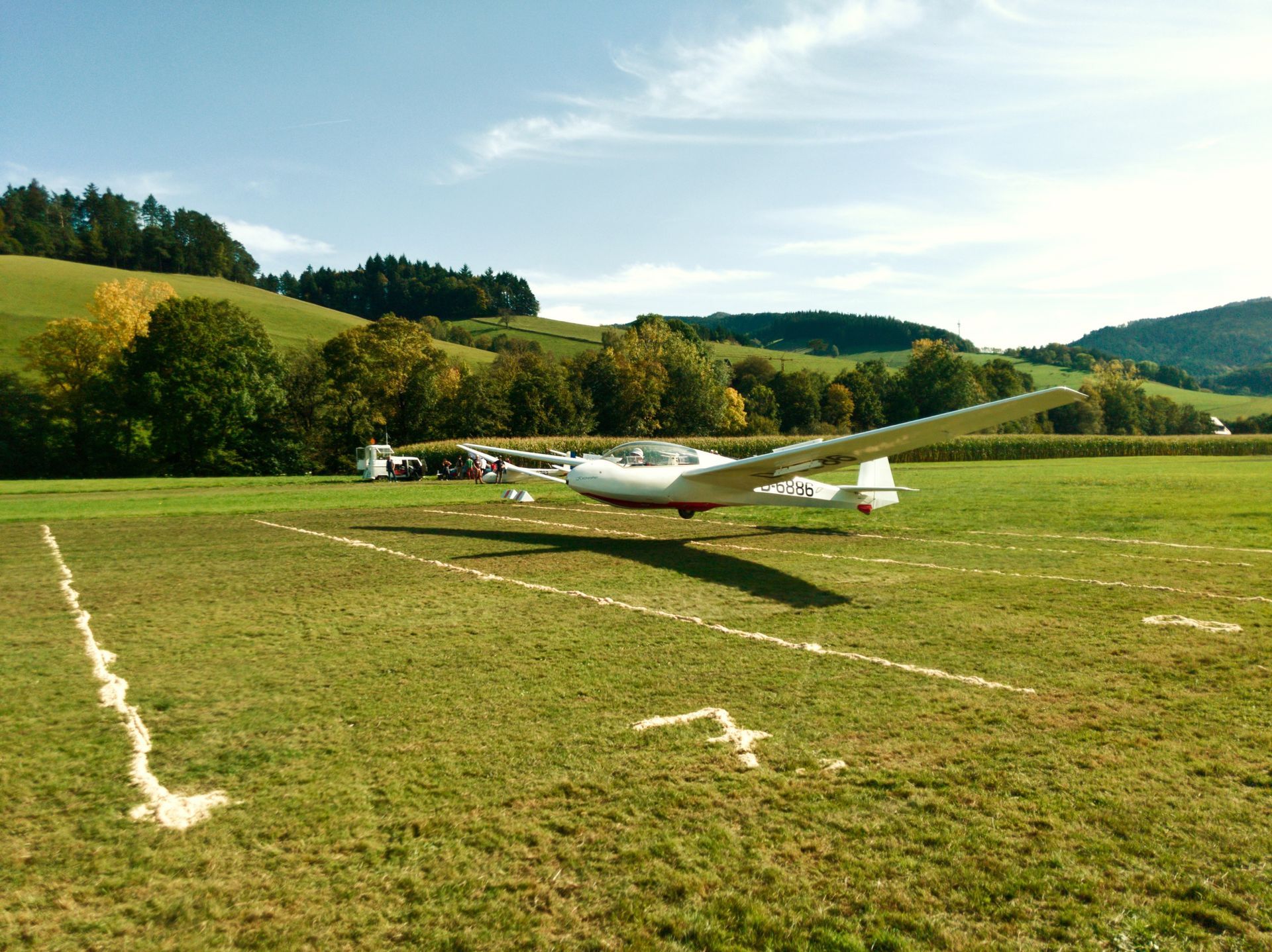 Segelflugzeug landet auf einer Grasfläche, auf die mit Sägespänen Felder gezeichnet sind.